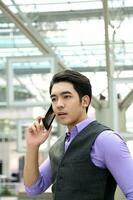 Southeast Asian young office business man wearing vest talk on phone thinking happy expression outdoor premises photo