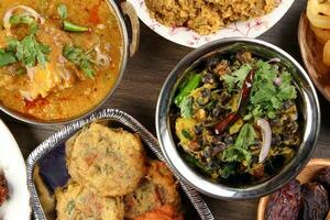 Bengali Iftar Ramadan breakfast spread ripe dates peep fried spicy piaju onion fitter eggplant tanpura potato chop haleem jilapi khichuri rice chana sola curry on rustic wooden table photo