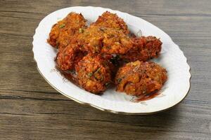 Deep fried piaju onion fitter bhajia on decorated ceramic plate over rustic wooden background photo