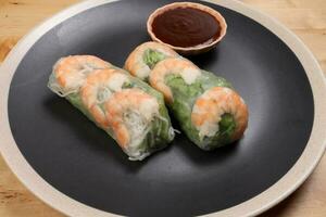 Vietnamese prawn shrimp see through rice paper spring roll green vegetable sauce on dark plate photo