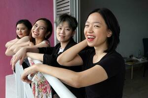 Young southeast asian woman group on balcony veranda standing side by side enjoying view talking happy looking photo