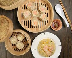 Prawn shrimp shaomai Xiao long bao dim sum dumpling chicken prawn fish seafood vegetable in bamboo steamer fried rice on plate sauce chopsticks soup spoon over rustic background photo