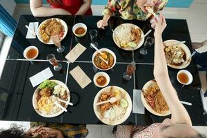 Young southeast asian woman group talk celebrate eating enjoying food rice curry noodle chicken drink cheers on dining table top view photo