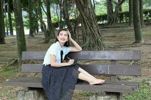 Young asian chinese woman outdoor on park bench hold file book folder read write see smile look photo