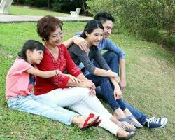 Sureste asiático multigeneracion familia padres hija abuela padre madre niño sentar Mira descanso hablar contento amor al aire libre parque foto