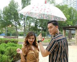 Young Asian Malay man woman outdoor green park walk talk discuss mingle under umbrella photo