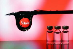 Small vaccine injection bottle transparent reflection refraction red led light background hypodermic syringe needle droplet type covid 19 vaccine photo