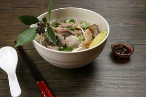 Vietnamese poh beef noodles soup broth with beef ball brisket tripe stomach parts been sprout thai basil lime in bowl on wooden table chopsticks spoon sauce photo