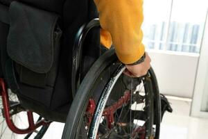 Young man south east Asian malay sitting on wheelchair look outside over balcony window . Paralyzed due to accident. Close up of hand and wheel photo