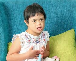 Southeast Asian small little girl child sitting on blue sofa look happy smile pose open arm happy hug sing. She have down syndrome photo