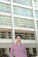 Young south east Asian middle woman business colleague in front of a tall building look forward at camera photo