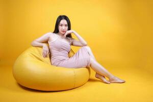 Beautiful young south east Asian woman sit on a yellow orange beanbag seat color background pose fashion style elegant beauty mood photo