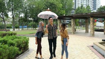 Young Asian Malay man woman outdoor green park walk talk discuss mingle under umbrella photo