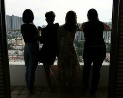 Young southeast asian woman group on balcony veranda standing side by side enjoying view talking happy looking silhouette photo