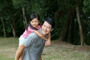South East Asian young Chinese father daughter parent child playing activity outdoor park riding on fathers back piggyback ride love photo