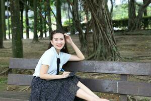 Young asian chinese woman outdoor on park bench hold file book folder read write see smile photo