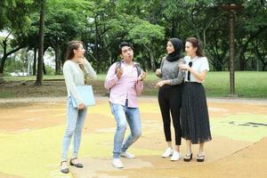 joven asiático malayo chino hombre mujer al aire libre parque caminar estar estudiar hablar discutir punto ordenador portátil archivo libro mochila divertido gracioso foto