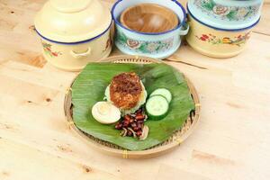 Nasi Lemak fragrant rice cooked in coconut milk served with sambal friend peanut anchovy boiled egg packed in banana leaf on round bamboo plate on wooden background pots containers photo