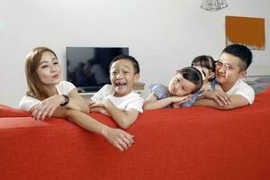 Parent mother father little child boy girl brother sister happy smile looking over the sofa photo