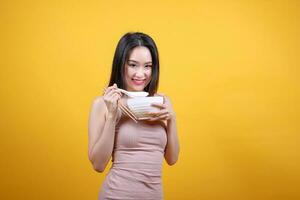 Beautiful young south east Asian woman holding chines empty chopstick Chinese soup spoon bowl utensil pretend acting posing see eat taste smell feed offer satisfaction yummy yellow orange background photo