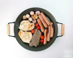 Mix meet pan chicken breast beef steak sausage tomato onion garlic oil fry grill on metal frying pan two wooden handle on white background photo