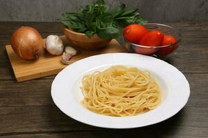 Cooked spaghetti on white plate with ingredients roma tomato glass bowl basil onion garlic wooden board recipe on table marble wall photo