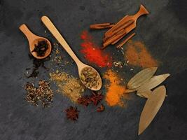 Mix variety spice cinnamon cardamom clove bay leaf wooden chilli cumin turmeric powered on black slate background photo