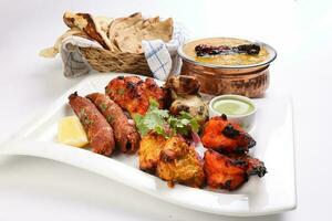 Mixed grill kebab chicken mutton beef prawn fish mint sauce lemon pickled onion bread basket chapati naan tandoori paratha dal lentil fry tadka copper pot on white dish over white background photo