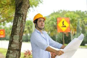 asiático hombre malayo trabajador ingeniero administración difícil sombrero la seguridad casco a construcción sitio leyendo viendo plan Plano Mira adelante foto