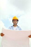 Asian man malay worker engineer management hard safety hat helmet at construction site reading seeing plan blue sky photo