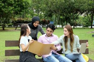 joven asiático malayo chino hombre mujer al aire libre parque libro archivo carpeta ordenador portátil computadora teléfono sentar estar estudiar mezclarse foto