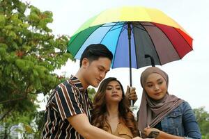 Young Asian Malay man woman outdoor green park walk talk discuss mingle under umbrella photo