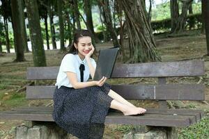 joven asiático chino mujer al aire libre parque instalaciones libro archivo carpeta ordenador portátil computadora teléfono sentar estar estudiar mezclarse foto