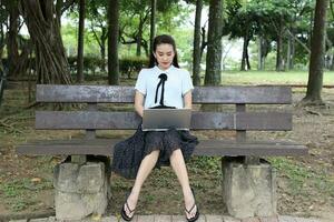 Young asian chinese woman outdoor on park bench use laptop computer think read look happy wonder smile look front down retro photo