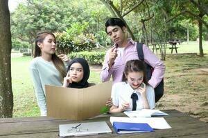 joven asiático malayo chino hombre mujer al aire libre parque libro archivo carpeta ordenador portátil computadora teléfono sentar estar estudiar mezclarse foto