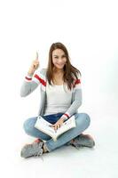 Yong Asian youth girl in casual dress sit on floor book on lap point up finger expression think idea on white background photo