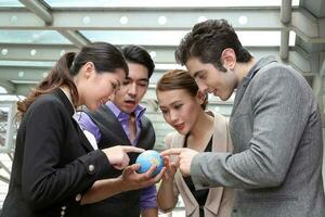 Southeast Asian Middle eastern Caucasian young office business man woman wearing vest suit holding globe world map on palm of hand discuss talk point show outdoor premises floor photo