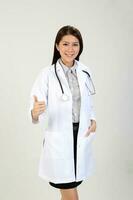 joven asiático hembra médico vistiendo delantal estetoscopio pulgares arriba foto