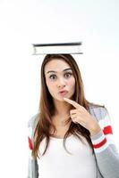 Yong Asian youth girl in casual dress balancing book on head look at camera finger on chin expression think shocked funny on white background photo