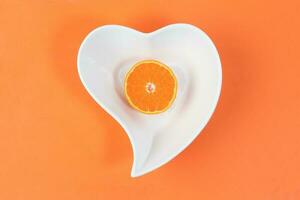 Mandarin Orange Fruit slice half juiced extracted on hart shape plate orange background photo