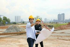 Man woman Malay Chinese worker engineer management hard safety hat helmet at construction site reading seeing plan photo