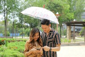 Young Asian Malay man woman outdoor green park walk talk discuss mingle under umbrella photo