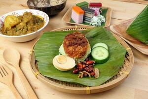 Nasi Lemak fragrant rice coconut milk with sambal friend peanut anchovy egg packed banana leaf round bamboo plate colorful nyonya kuih sweet desert palm leaf plate on wooden background photo