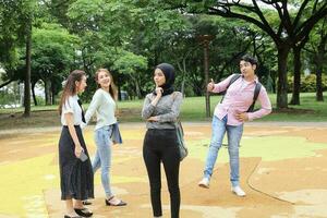 joven asiático malayo chino hombre mujer al aire libre parque caminar estar estudiar hablar discutir punto ordenador portátil archivo libro mochila foto