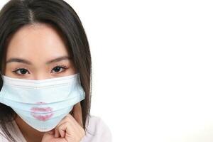 hermosa joven sur este asiático mujer vistiendo azul Tres capa anti virus quirúrgico cara máscara lápiz labial labios Beso firmar marca en blanco antecedentes Mira adelante foto