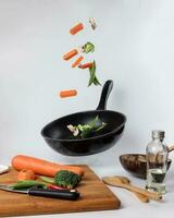 chopped sliced diced carrot broccoli white button mushroom red chili flying dropping gravity defying on floating elevated metal frying pan cooking board bowl oil knife on white background photo