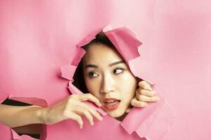 Young beautiful Asian woman expression through torn paper hole photo