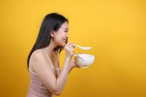 Beautiful young south east Asian woman holding chines empty chopstick Chinese soup spoon bowl utensil pretend acting posing see eat taste smell feed offer satisfaction yummy yellow orange background photo