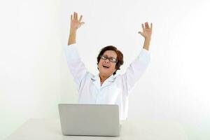 Elderly asian Chinese female doctor on white background wearing white apron notebook computer happy joy hand in air photo