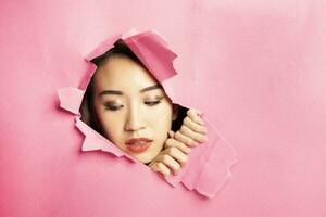 joven hermosa asiático mujer expresión mediante Rasgado papel agujero foto